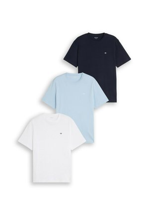 Trois t-shirts unis à manches courtes en bleu marine, bleu clair et blanc, chacun avec un petit logo œil brodé sur la poitrine.