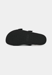 Μαύρη σανδάλι με υφή από καουτσούκ, με διπλές ρυθμιζόμενες λουρίδες και επίπεδη σχεδίαση για ευκολία στη χρήση.