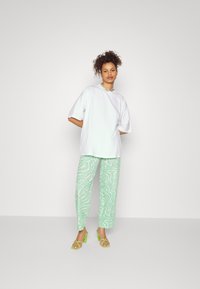 T-shirt oversized branco, calças largas com padrão verde e sandálias de salto alto verde brilhante. Inclui um colar simples como acessório.