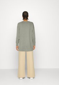 Maglione a maniche lunghe dalla vestibilità comoda in maglia grigia chiara, abbinato a pantaloni beige larghi. Texture liscia, design minimalista.