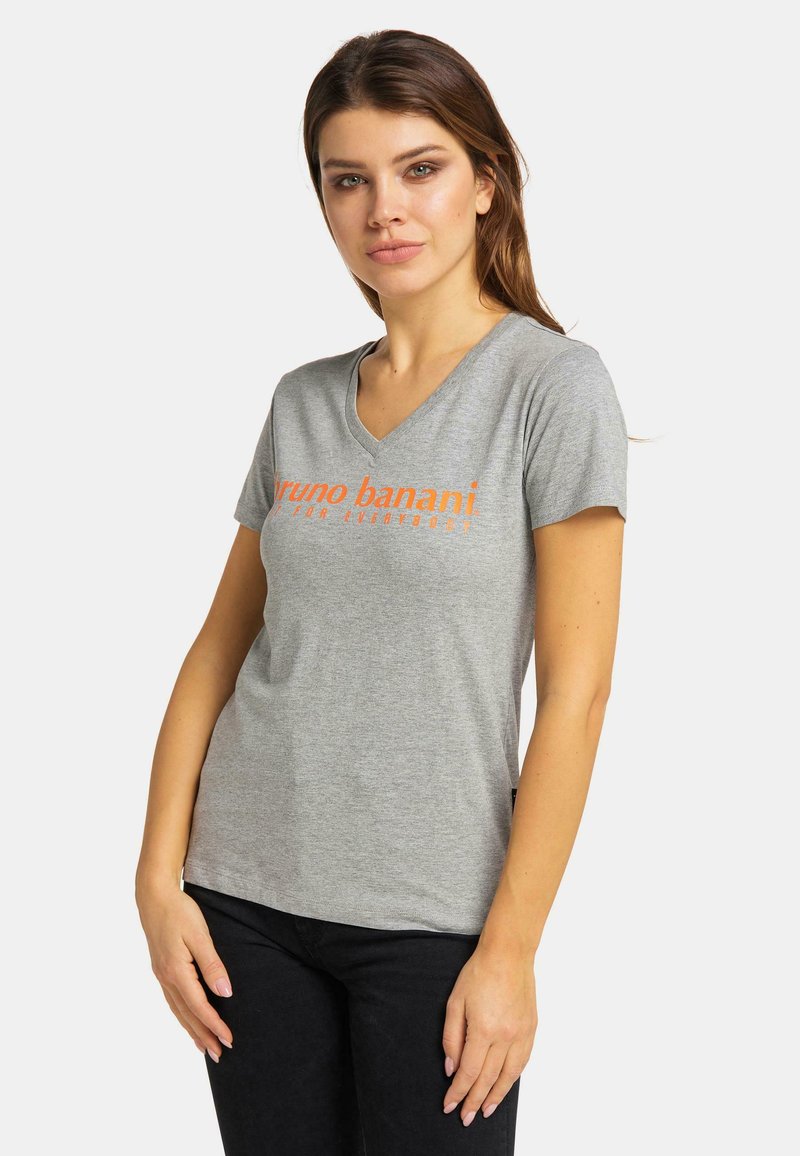 Grå kortärmad t-shirt med v-ringning och orange tryckt text. Mjukt tyg och avslappnad passform, bärs med svarta byxor.