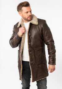 Abrigo de cuero marrón con cuello de borreguillo, con cierres de botones, dos bolsillos frontales y superficie texturizada. Diseñado para proporcionar calor.