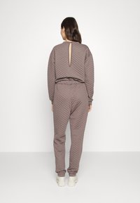 Kviltad, långärmad, brun loungewear-set med en nyckelhålsklippning baktill och elastisk midja; matchas med ljusa skor.