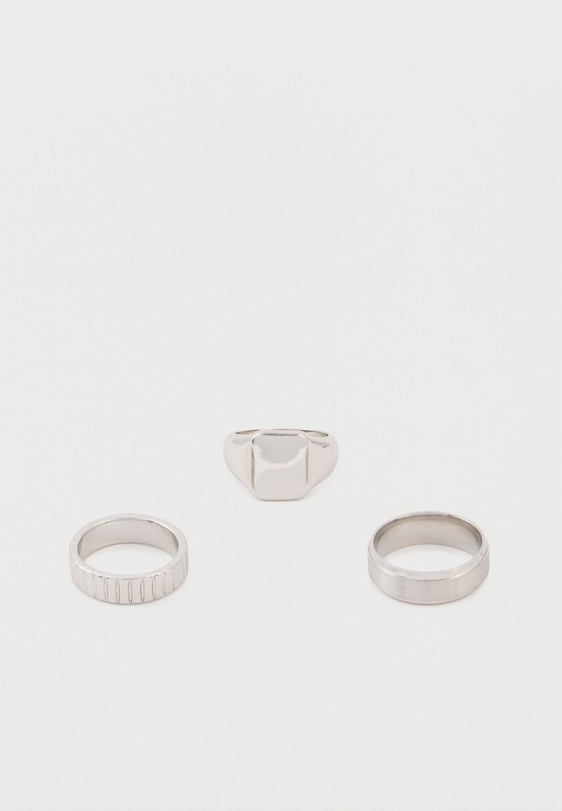 Τρία ασημένια δαχτυλίδια σε λευκή επιφάνεια: το ένα με χαραγμένες κάθετες γραμμές, ένα απλό δαχτυλίδι και ένα σινιέ δαχτυλίδι με επίπεδη ορθογώνια επιφάνεια.
