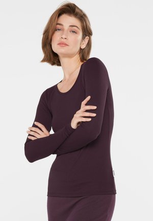 Langärmliges lila Oberteil aus weichem, dehnbarem Stoff mit Rundhalsausschnitt und taillierter Silhouette. Mit kleinem Logo am Saum.