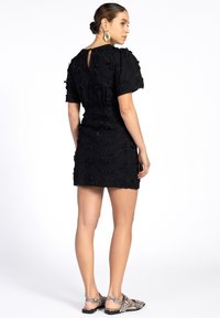 Schwarzes, mit Blumenstickerei verziertes Minikleid mit kurzen Puffärmeln, Schlüsselrücken-Detail, strukturiertem Stoff und Schuhen im Schwarz-Weiß-Schlangenprint.