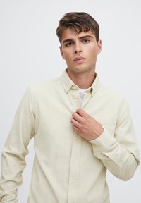 Light yellow button-up shirt with a collar, long sleeves, and a front pocket. The fabric appears textured and durable.