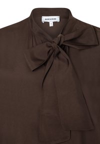 Bruine blouse met een zachte, gladde textuur, met een gestrikte strik bij de kraag en een label met "MORE & MORE" met maat 36.