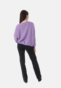 Paarse gebreide trui met een ontspannen pasvorm en een textuurpatroon, gecombineerd met zwarte rechte jeans. De outfit wordt van achteren bekeken.