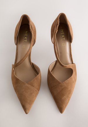 Braune Wildleder-Absätze mit spitzer Zehenpartie, versehen mit gekreuzten Riemen über dem Obermaterial und einem glatten Innenfutter. Goldenes Markenlogo sichtbar.