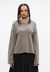 Jasnoszary sweter wykonany z miękkiej, teksturowanej tkaniny. Posiada okrągły dekolt, opadające ramiona oraz luźny krój. Długie rękawy z podwiniętymi mankietami.