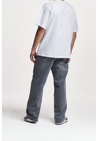 Bílé bavlněné tričko spojené se šedými džínovými kalhotami. Kalhoty mají volný střih a viditelné kapsy, doplněné černo-bílými teniskami.