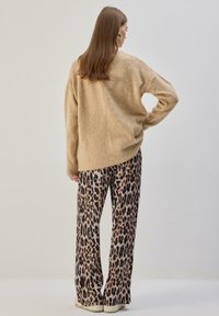 Beežikarva karvane kampsun pikkade varrukatega, kombineeritud lahtiste leopardimustriliste pükstega. Pükstel on tumedate laikudega muster heledamal taustal.