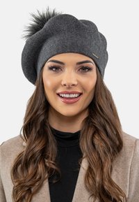 Beret gris en tissu doux, ornée d'un pompon moelleux sur le dessus et d'un subtil accent métallique. Texture lisse avec une forme arrondie.
