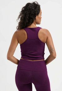 Lila Tanktop mit Racerback-Design und glatter Textur. Verfügt über eine figurbetonte Silhouette, getragen zu passenden lila hoch taillierten Leggings.