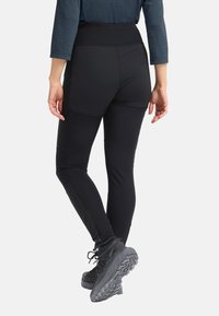 Leggings sportivi neri con vita alta e dettagli con cerniera alle caviglie, realizzati in tessuto elasticizzato e liscio. Indossati con scarpe da trekking grigie.