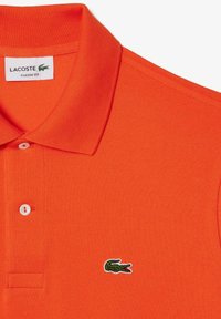 Camisa polo naranja en un corte clásico, con un tejido texturizado, cuello corto y un logo de cocodrilo bordado en verde en el pecho.
