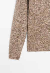 Maglione lavorato a maglia di un caldo colore beige con un motivo testurizzato e melangiato. Caratterizzato da maniche lunghe e polsini e orlo a costine.