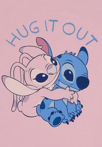 Camiseta de color rosa claro con dos personajes de dibujos animados, uno rosa con orejas largas y uno azul, abrazándose. El texto arriba dice "ABRÁZATE".