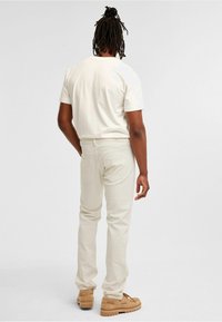 Kreemivärvi lühikeste varrukatega t-särk ja sobivad slim-fit püksid. Mugav kangas, millel on sile tekstuur. Igapäevased jalatsid heledas pruunis.