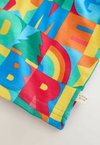 Värikäs puuvillakankaan kuvio, jossa geometrisia muotoja, kirjaimia, puita ja sateenkaaria sinisen, punaisen, keltaisen ja vihreän sävyissä. Pienessä merkkilapussa lukee "Little Bird".