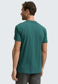 Zielona koszulka z krótkim rękawem, wykonana z miękkiego materiału, z okrągłym dekoltem i luźnym krojem. Gładka faktura bez widocznych wzorów.