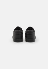 Black athletic shoes with smooth leather upper, textured nylon accents, and rubber sole. Rear view highlights padded collar and contrasting stitching.