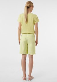 Żółta bluzka z krótkim rękawem o fakturowanym wykończeniu, zestawiona z pasującymi żółtymi szortami. Minimalistyczny design, miękki materiał i długość do połowy uda.