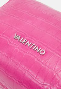 Růžové kožené psaníčko s krokodýlím vzorem, výrazně zdobené stříbrným logem "Valentino". Obdélníkový tvar.