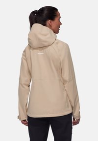 Beige Damenjacke mit Kapuze, aus glattem Material, mit einem schlichten Design und einem Logo auf dem Rücken. Eng anliegende Bündchen.