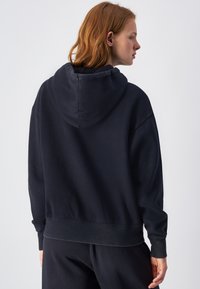 Sudadera de color azul marino oscuro hecha de tela suave con un corte relajado, con capucha ajustable y puños acanalados. Diseño minimalista, sin logotipos visibles.