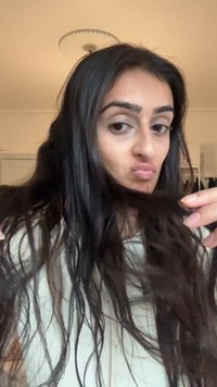 Lang, mørkebrun hår med en lett bølging, holdt i hendene. Bakgrunnen har lyse vegger og skapdører. En nøytral genser er iført.