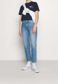 Laivastonsininen t-paita, valkoinen neule sidottuna olkapäiden ympärille, vaaleansiniset suoralahkeiset farkut ja valkoiset korkeavartiset tennarit.