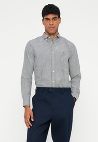 Koszula w paski w kolorze granatowym i białym, z kołnierzykiem, długimi rękawami i małym logo na piersi, zestawiona z granatowymi spodniami.