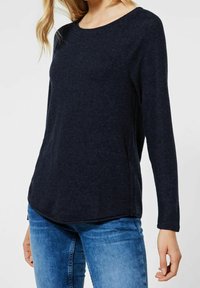 Pull-over long à manches en marine en tissu doux avec un col rond, présentant un ourlet légèrement incurvé et une coupe décontractée. À porter avec un jean.