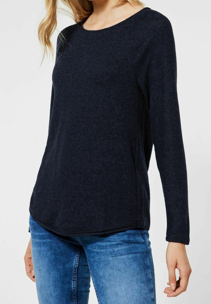 Pull-over long à manches en marine en tissu doux avec un col rond, présentant un ourlet légèrement incurvé et une coupe décontractée. À porter avec un jean.