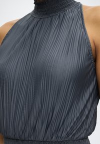 Haut sans manches gris foncé plissé avec col haut froncé et taille élastique sur une personne.