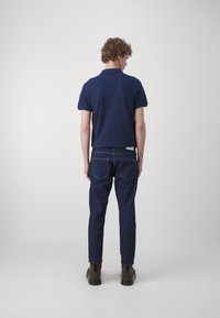 Marineblå polo med korte ermer, kombinert med mørkeblå jeans. Antrekket har rett snitt og synlige sømdetaljer. Brune støvler fullfører utseendet.