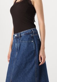 Denim skirt featuring a high waist, front pockets, and a light blue wash. Accompanied by a black tank top with lace trim.