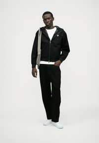 Čierna zipová bunda s kapucňou, skombinovaná s bielym tričkom, čiernymi nohavicami a bielymi topánkami. Vyznačuje sa ľahkým, neformálnym dizajnom.