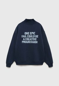 Námornícky sveter vystavený na plochu, so výrazným svetlomodrým textom na zadnej strane, ktorý hovorí: "Jedna epická porážka môže byť kreatívnym pokrokom."