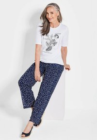 Weißes T-Shirt mit floralem Druck und kurzen Ärmeln, kombiniert mit navyblauen Hose mit Punkten, die eine lockere Passform und ein weiches Material aufweist.