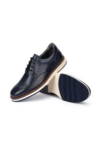Un paio di scarpe da uomo eleganti in pelle blu scuro con lacci, una mostra la parte superiore liscia, l'altra mostra la suola in gomma blu con un motivo di battistrada.