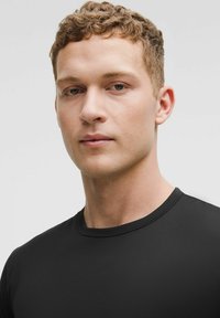 Črna kratkosleeva majica iz gladkega materiala, s krožno ovratnikom in prilegajočim krojem. Preprost dizajn brez vzorcev ali dodatkov.