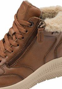 Hnědé kožené kotníkové boty s umělou kožešinou, šněrováním a bočním zipem. Disponují texturovanou gumovou podrážkou se světlými akcenty.