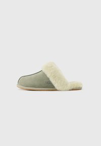 Zachte groene suede slof met een crèmekleurige pluche voering en afwerking, voorzien van het UGG-logo aan de zijkant, met een platte zool.