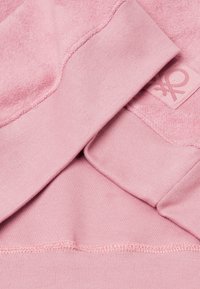 Różowa bluza z futrzastą teksturą w górnej części i prążkowanymi mankietami. Zawiera naszywkę z logo w tym samym kolorze.