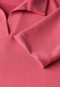 Różowa koszulka polo z złożonym kołnierzykiem i krótkimi rękawami, wykonana z gładkiej tkaniny z delikatnymi detalami przeszycia na krawędzi.