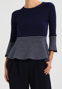 Top péplum bleu marine à manches trois-quarts, avec une section inférieure rayée en blanc et bleu marine. Confectionné dans un tissu côtelé.