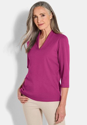 Fuchsia v-hals top met driekwartmouwen, gemaakt van een gladde stof, aansluitend ontwerp en een lichte val, gecombineerd met beige broek.